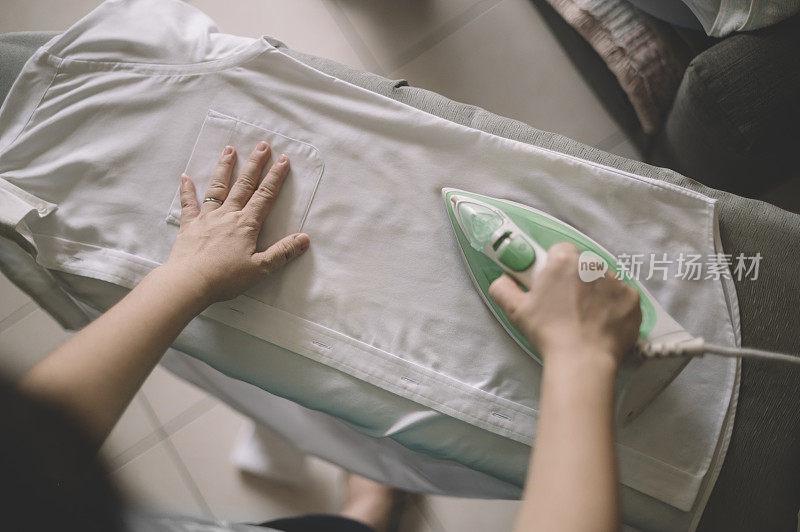 an asian chinese mid adult ironing his button down white shirt high angle view